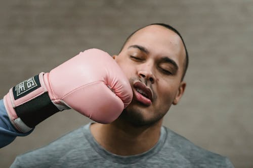 Crop unrecognizable fighter in protective glove punching in face of young ethnic male opponent during boxing workout