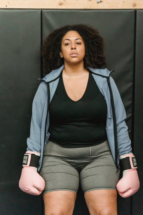 Confident young African American obese woman standing near wall after boxing workout