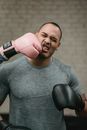 Muscular young ethnic male boxer in activewear receiving heavy punch on face from crop anonymous fighter