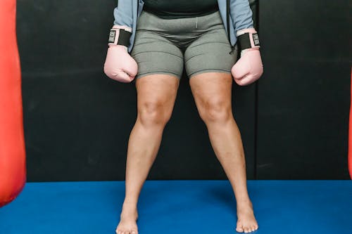 Crop anonymous barefooted overweight lady in activewear and boxing gloves standing in ring before workout