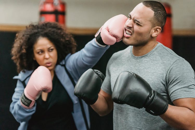 Serious Black Woman Hitting Ethnic Male Trainer During Boxing Workout