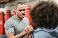 Muscular young ethnic male trainer shaking hand of unrecognizable African American female before workout in gym