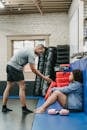 Full body side view of muscular black personal coach reaching out hand to African American female while training in gym