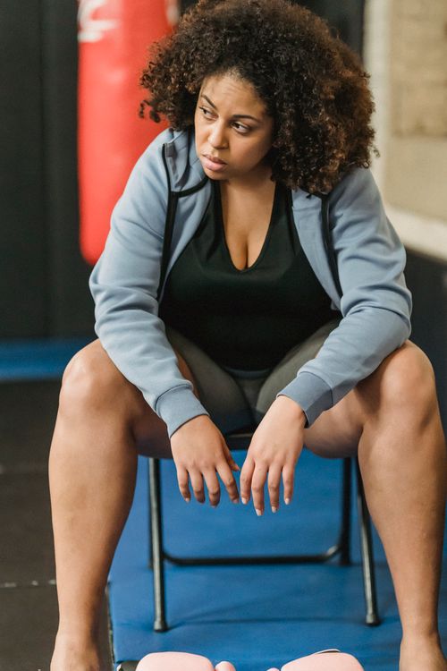 Free Calm plus size African American female in sportswear looking away while sitting on chair near boxing gloves during training in gym Stock Photo