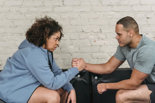 Two individuals engage in an intense arm wrestling match indoors, focusing on strength and determination.