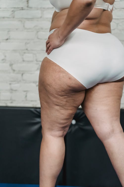 Side view of unrecognizable overweight female in underwear standing with hand on hip near white brick wall and black mat
