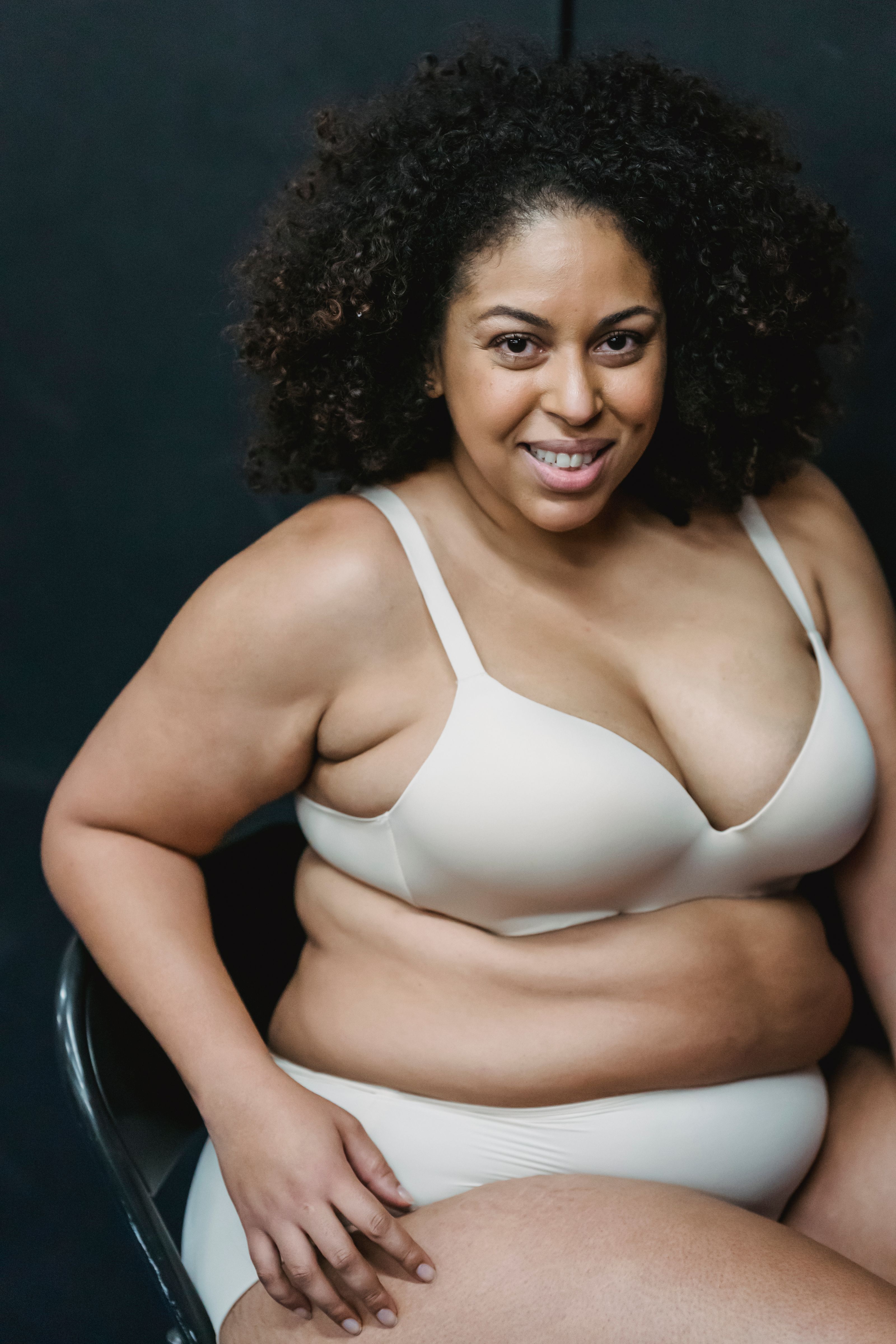 Mulher plus size com cabelo cacheado sorrindo confiantemente em um estúdio, promovendo a positividade corporal.