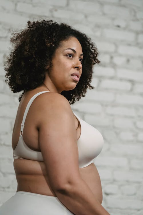 Confident adult plump ethnic female in white underwear in bright room near white brick wall