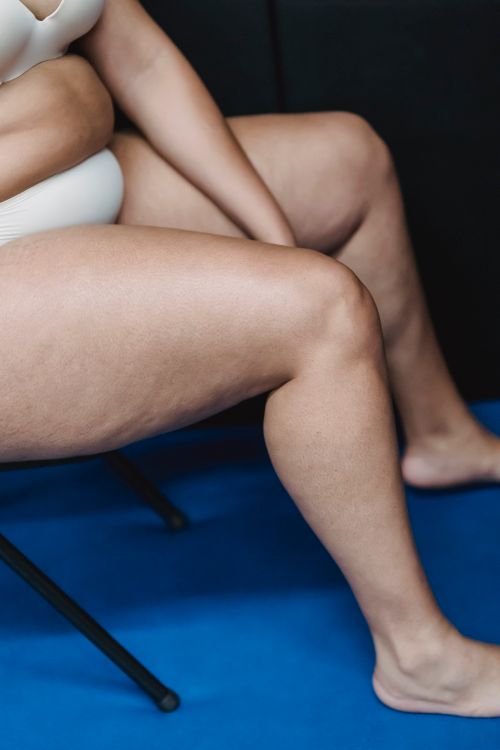 Free Crop faceless plump female in white underwear sitting on chair on blue floor in light studio on black background Stock Photo
