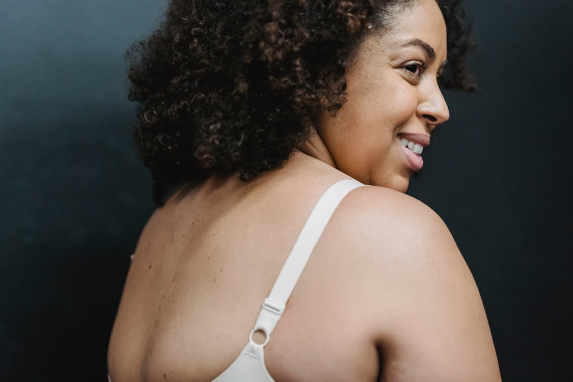 Positive adult plump ethnic female in white bra in bright studio on gray background