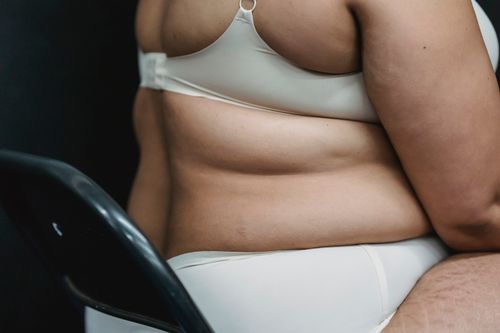 Free Crop faceless plump woman in white underwear sitting on chair in light studio on dark background Stock Photo