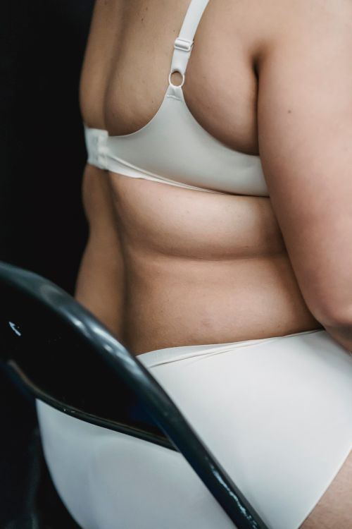 Free Crop unrecognizable plump lady in white underwear sitting on chair in light studio on black background Stock Photo