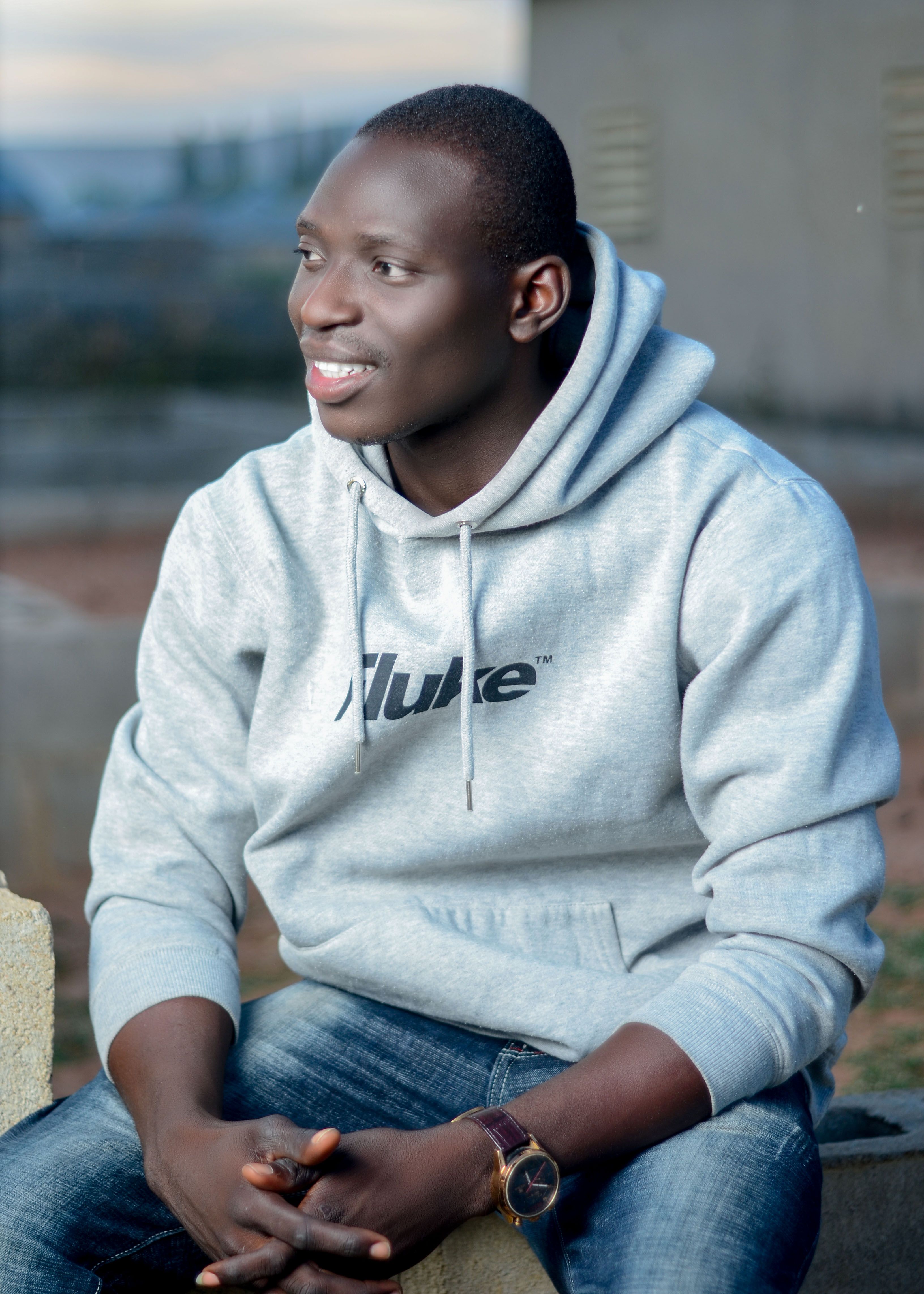 Outdoor portrait of a smiling man in casual clothing, sitting comfortably.
