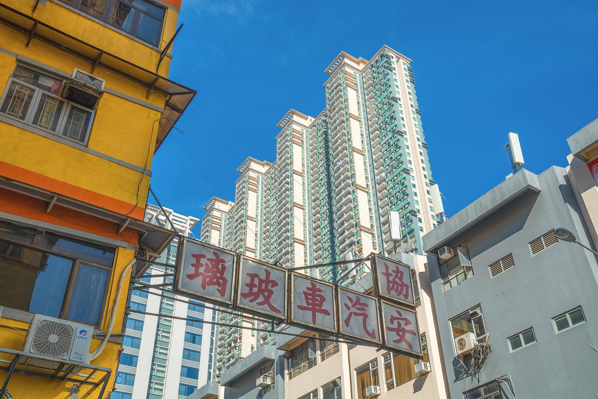 Low angle view of vibrant high-rise buildings in downtown Hong Kong under a clear blue sky.