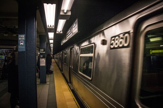 Busy New York subway station with train arriving and commuters waiting on platform.