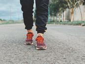 Crop legs of person in sneakers and sportswear standing on asphalt road on blurred background of green trees in countryside