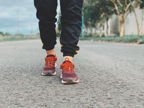 Free Crop legs of person in sneakers and sportswear standing on asphalt road on blurred background of green trees in countryside Stock Photo