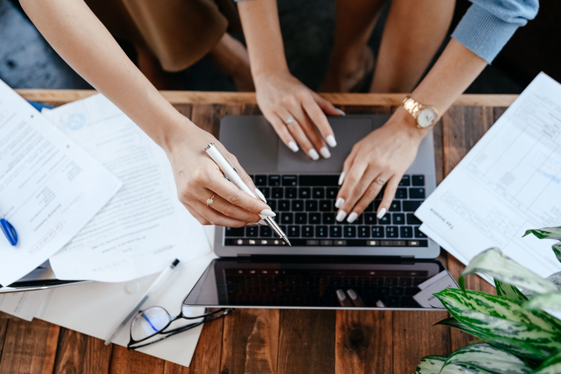 Top view of anonymous women browsing modern netbook while sitting at wooden desk with stack and documents during work in office