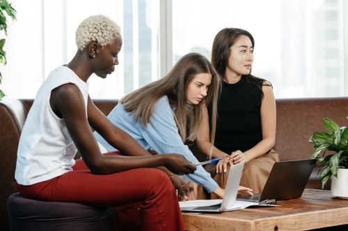 Free Side view of multiracial female coworkers typing on netbooks while sitting at table on couch during teamwork in modern office Stock Photo
