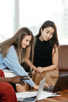 Diverse team collaboratively working on a project with laptops and documents in a modern office.