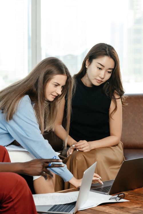 Free Focused diverse female coworkers surfing netbook while sitting on couch near table during work in office with anonymous black colleague Stock Photo