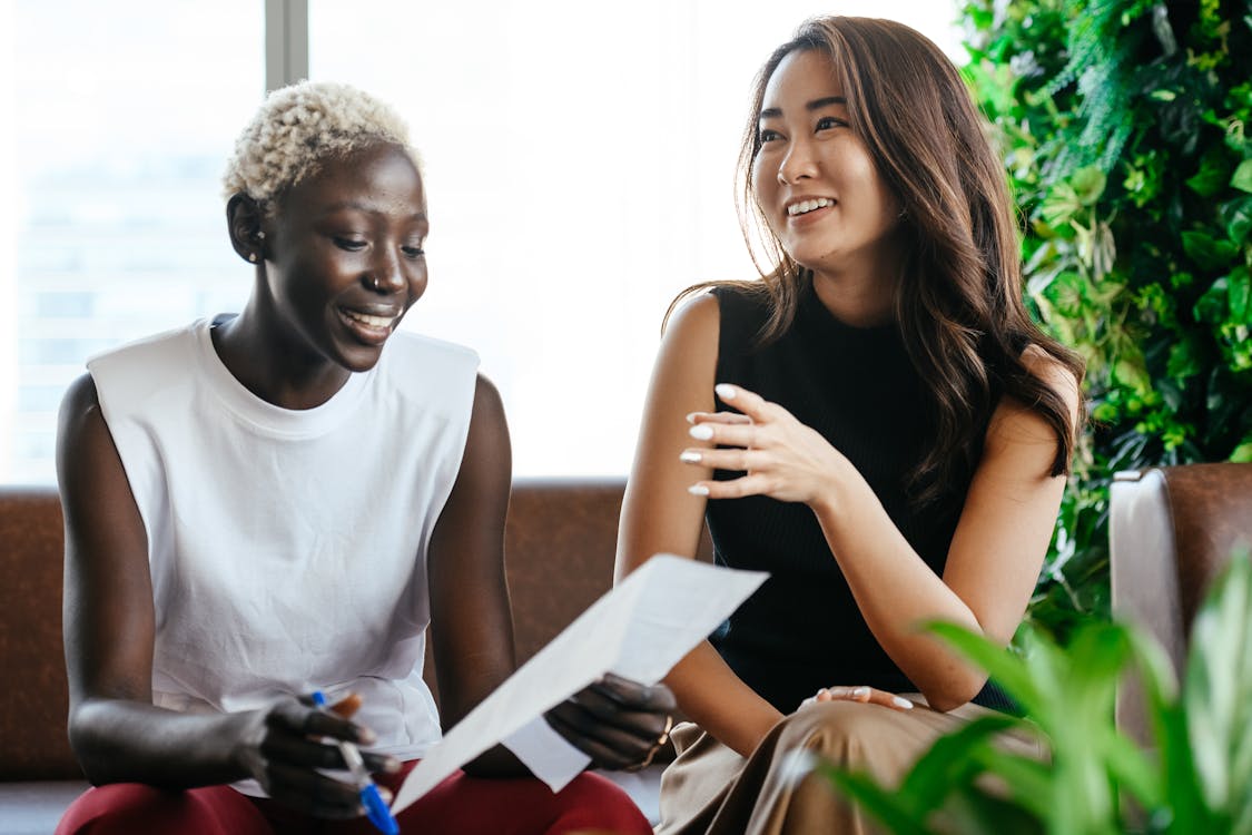 Free Multiethnic happy smiling women checking papers while speaking in comfortable conference hall in daytime Stock Photo