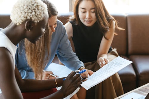 Free Young multiethnic crop women working on important document while discussing project in office in daytime Stock Photo