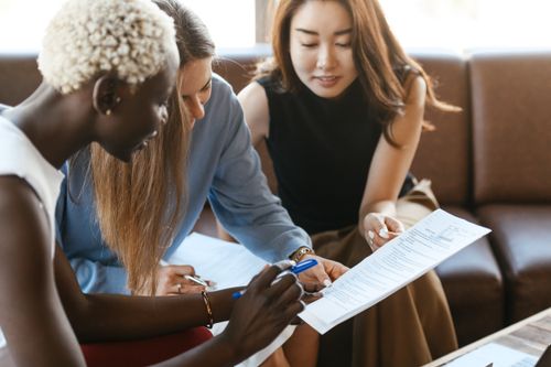 Free Young multiethnic crop women working on important document while discussing project in office in daytime Stock Photo