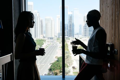 Free Side view of diverse women with coffee discussing strategy of work in office with large window in daytime Stock Photo