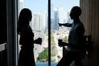 Side view of anonymous diverse business partners with coffee talking about job while admiring tall contemporary buildings of large megapolis