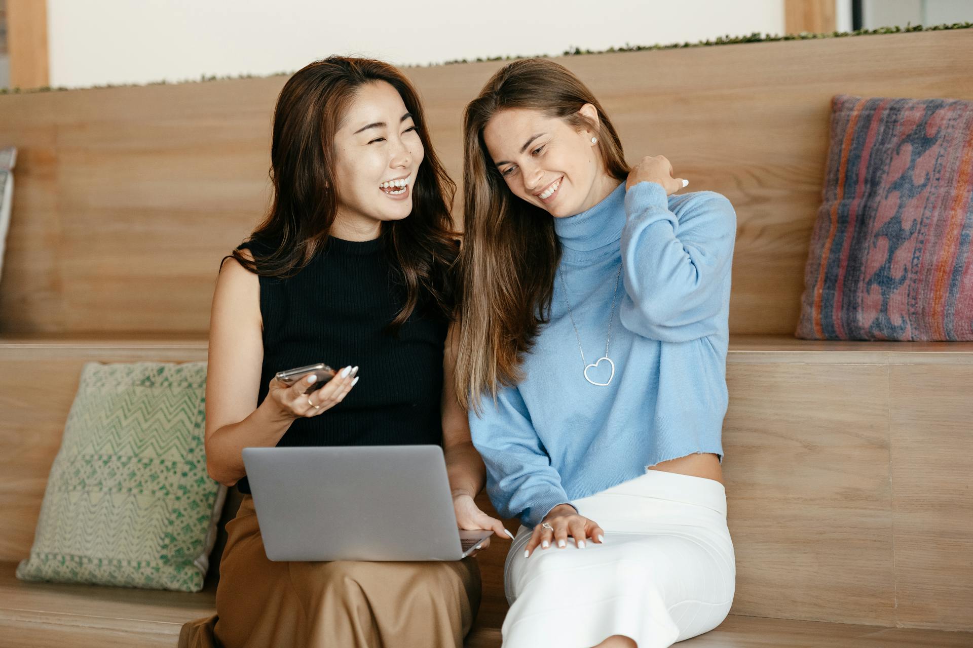 Cheerful young multiracial friends smiling and surfing internet on netbook while using mobile phone