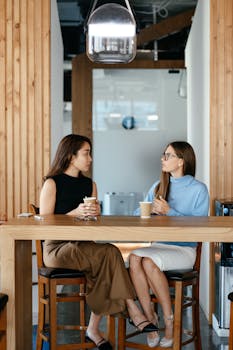 Two diverse professional women enjoying a conversation over coffee in a modern café setting.