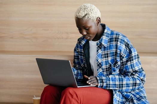 Young serious African American female in trendy blue checkered shirt using netbook and freelancing