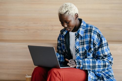 Free Young serious African American female in trendy blue checkered shirt using netbook and freelancing Stock Photo