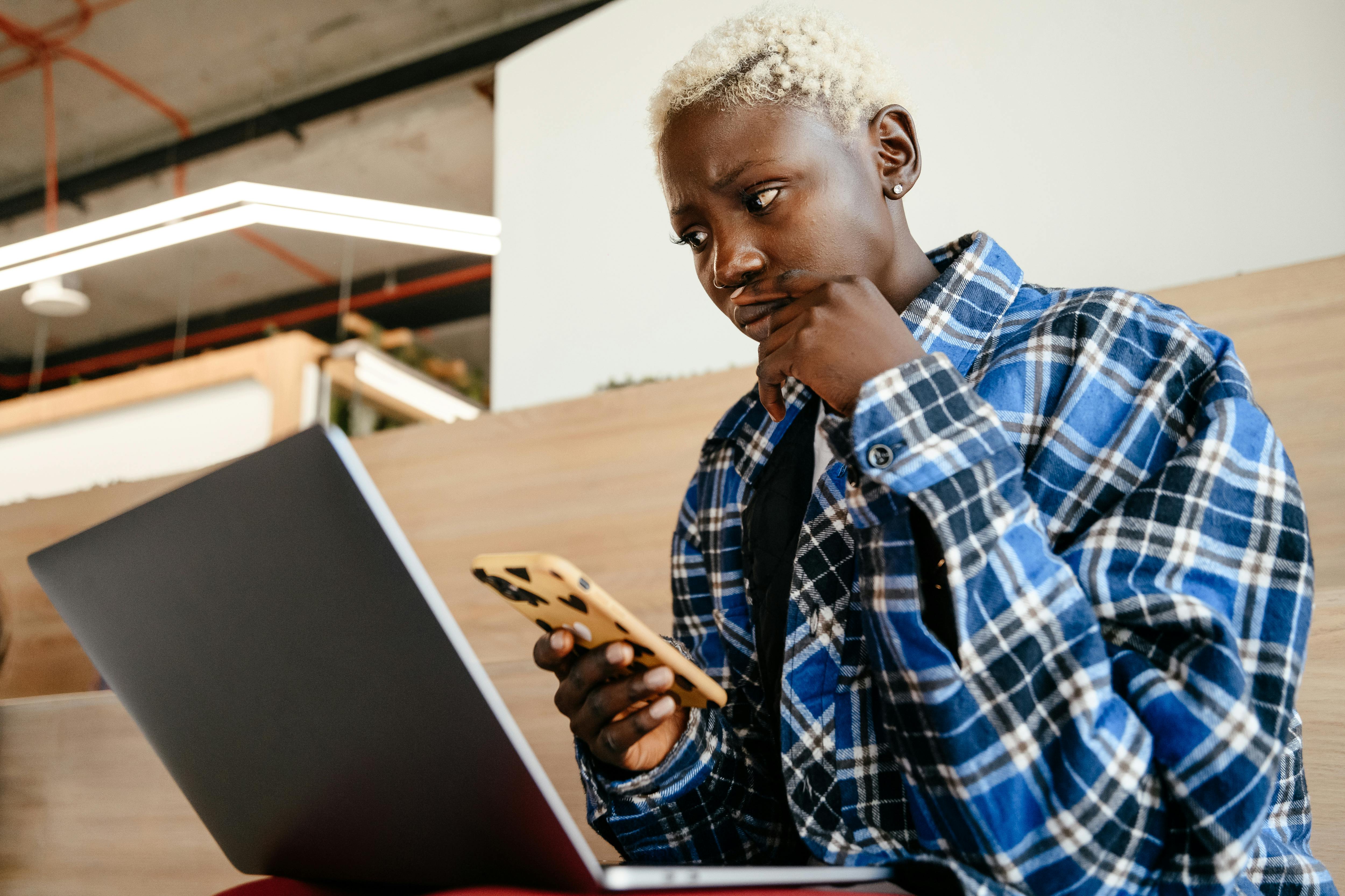 thoughtful black woman using smartphone and laptop