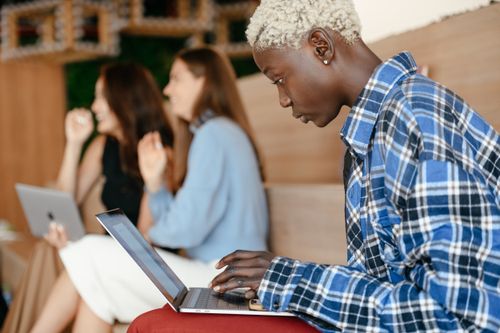 Free Side view of concentrated crop African American female in trendy casual blue checkered shirt working with netbook near multiethnic partners Stock Photo