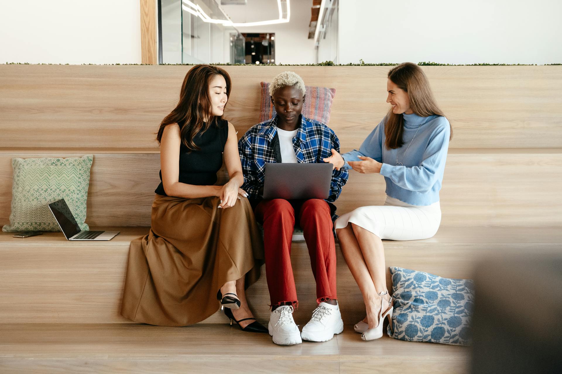 A multiethnic group of women collaborating on a project indoors, using a laptop and smiling.