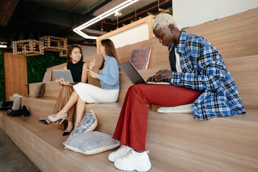 Multiracial women using netbooks while speaking on wooden steps of contemporary workspace in daytime
