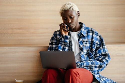 Free Serious African American female in trendy blue checkered shirt speaking on mobile phone while browsing netbook Stock Photo