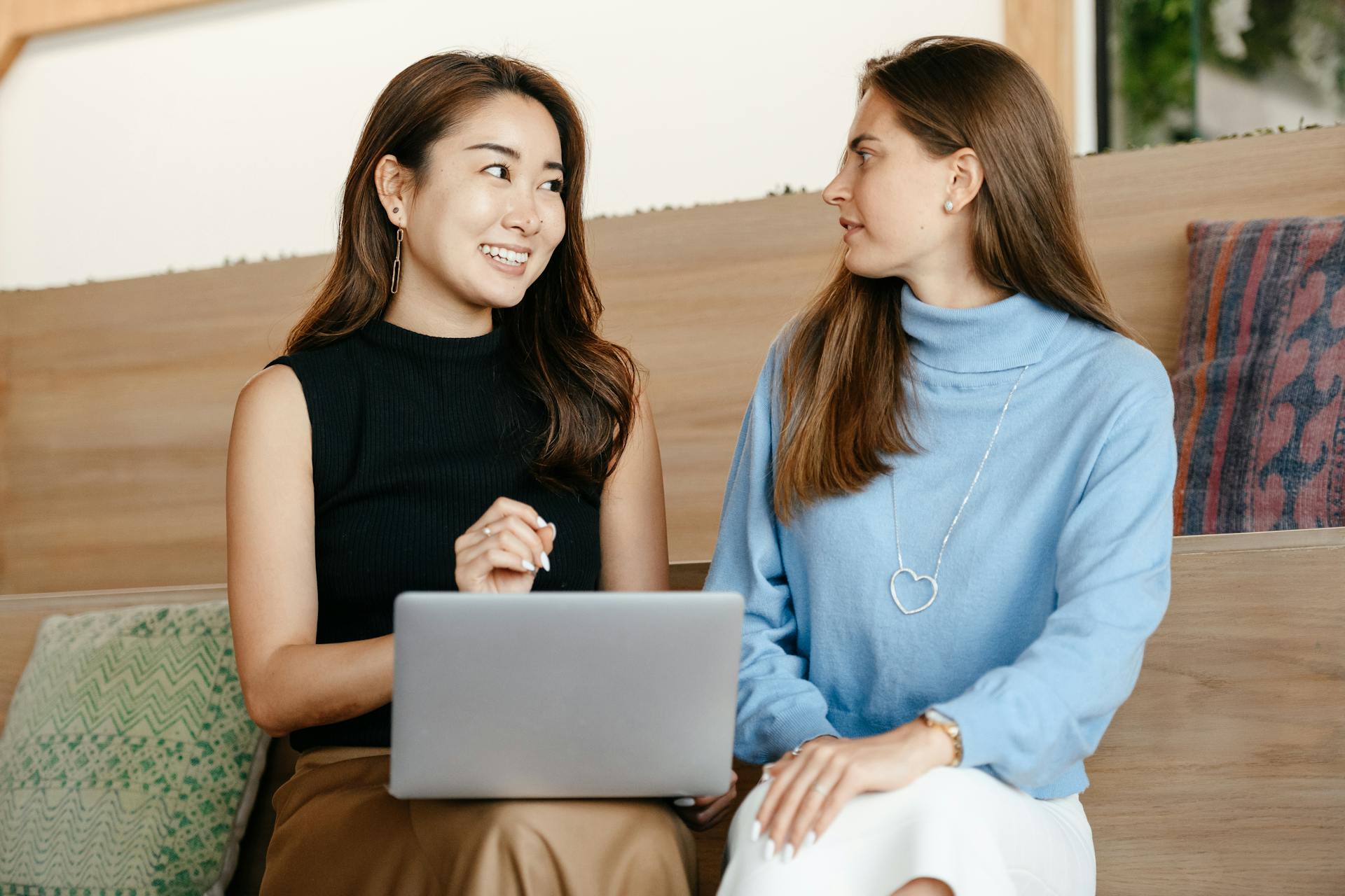 Two diverse women having a cheerful business discussion using a laptop indoors.