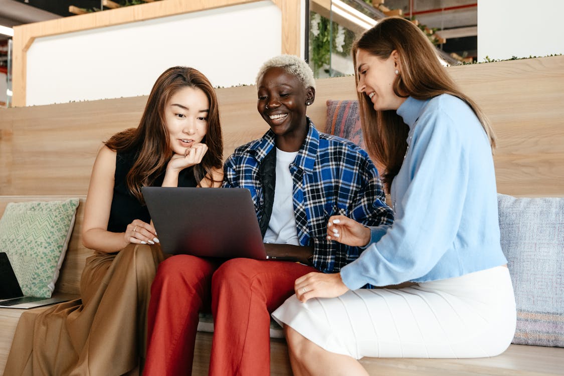 Free Group of happy trendy multiethnic women surfing internet on netbook while talking and smiling Stock Photo