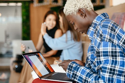 Black woman with laptop texting message on smartphone among colleagues