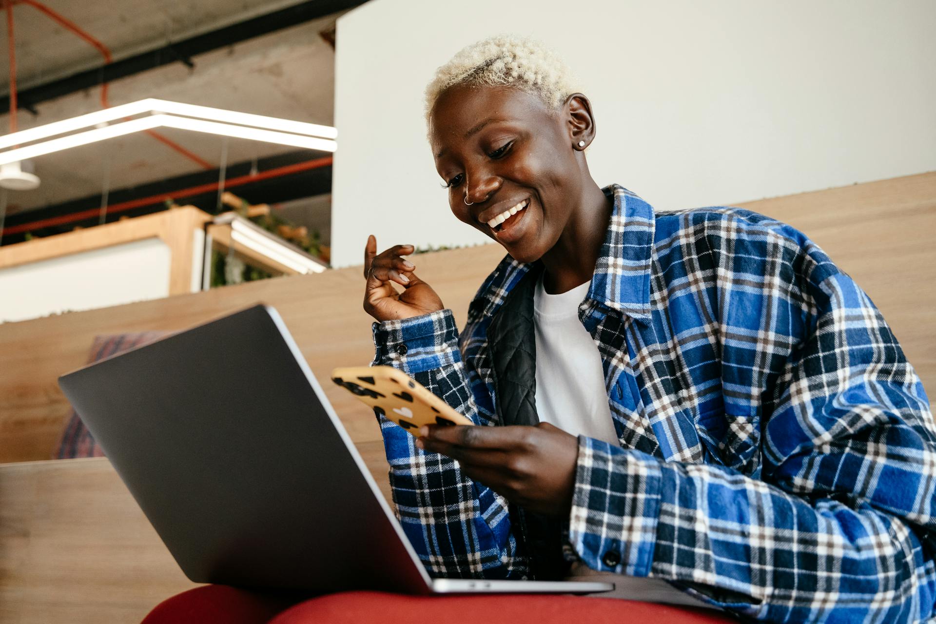 From below of cheerful African American female smiling and texting message on mobile phone while working with netbook