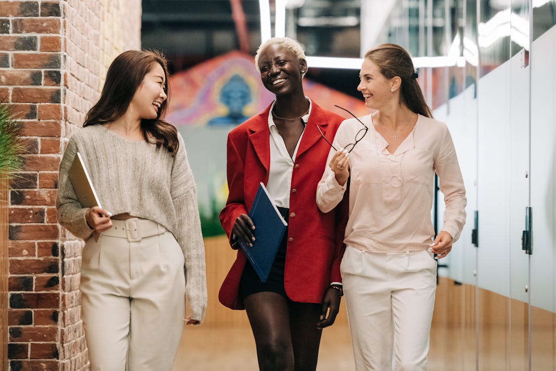 Free Group of young glad businesswomen in trendy elegant outfits smiling and discussing business strategy in contemporary workspace Stock Photo