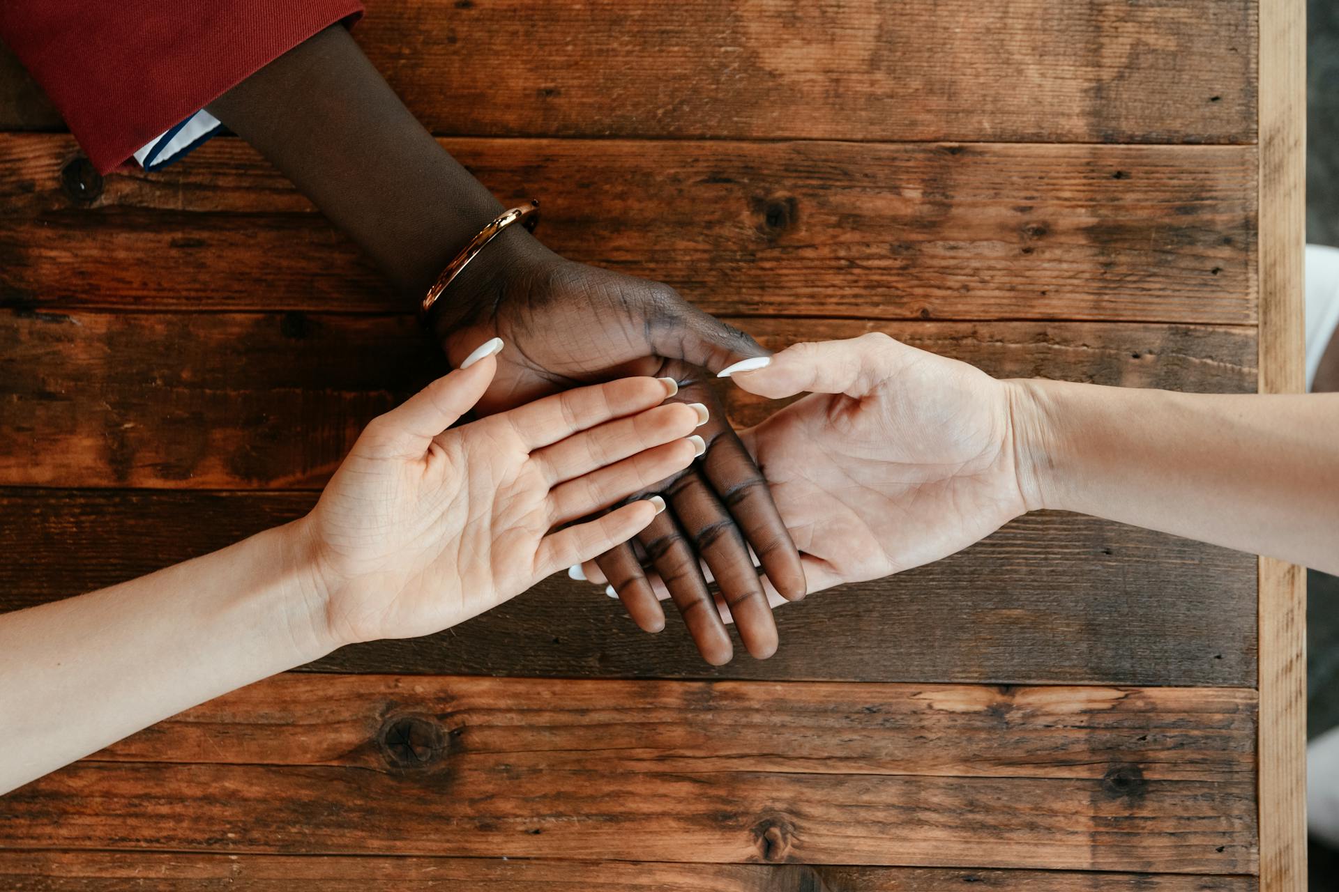 Top view of diverse hands joining together in harmony on a wooden table, symbolizing unity.