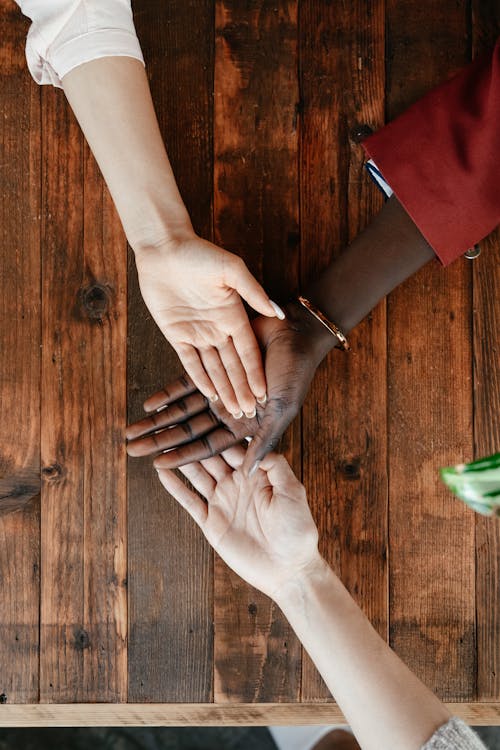 Free Top view of crop unrecognizable women stacking hands together on wooden surface in daytime Stock Photo