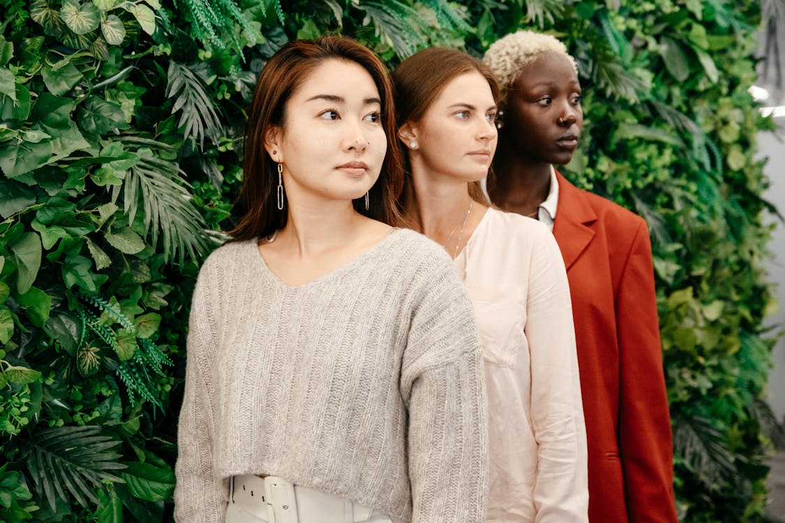 Free Row of modern multiethnic women looking away near bushes with fresh verdant leaves in garden in daytime Stock Photo
