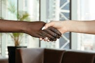 Crop anonymous diverse women shaking hands together on blurred background of contemporary office