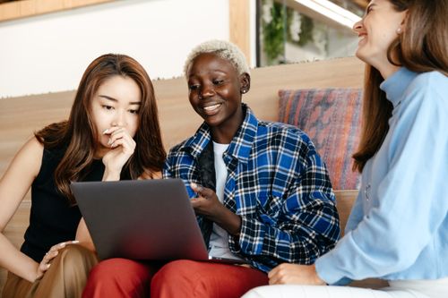 Free Glad young diverse ambitious coworkers smiling and solving project while using netbook together in daytime Stock Photo