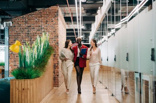 Free Full body of multiracial happy businesswomen in elegant suits smiling and talking about work in convenient modern office Stock Photo